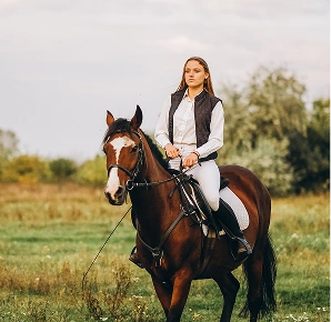 Young woman riding chestnut horse in green meadow